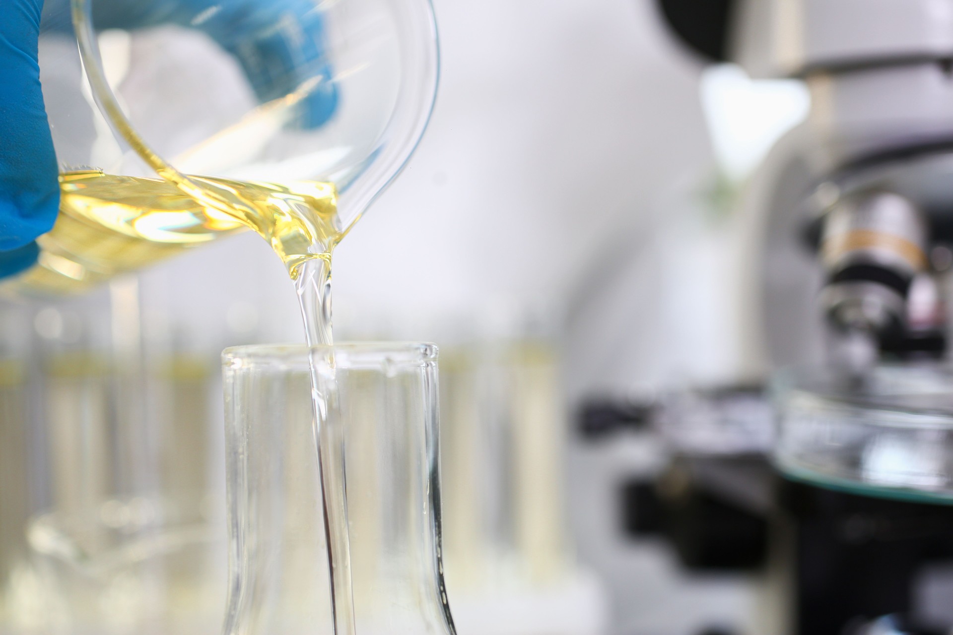 Wissenschaftler Hand trägt Schutzhandschuhe gießen einige gelbe Flüssigkeit im Labor